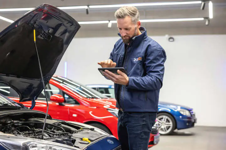 Werkstattmitarbeiter schaut sich das Auto von außen an – Tablet in der Hand.