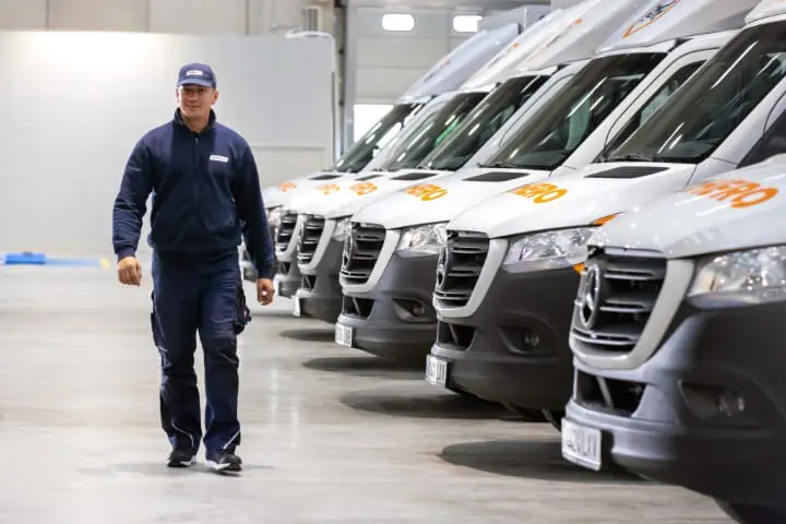 Drie mensen staan lachend voor een glazen vrachtwagen van Autohero. 😊