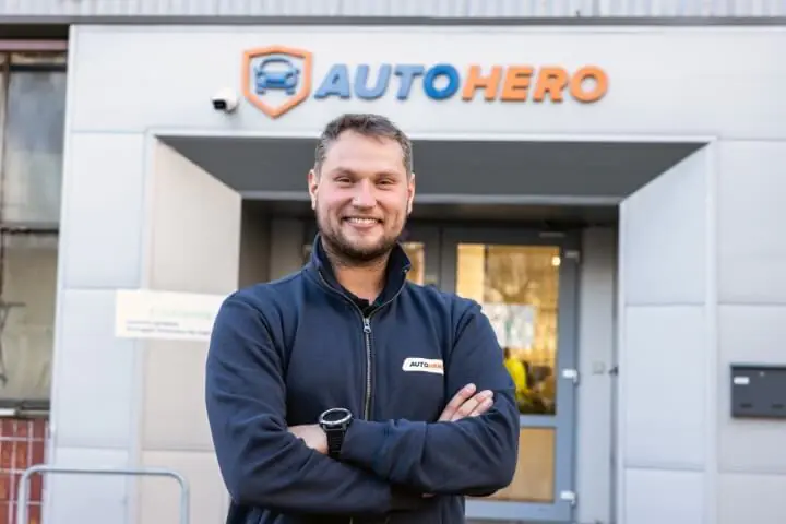 Een man in Autohero-kleding staat in een werkplaats, met auto's op de achtergrond.