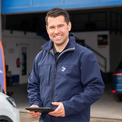 Mitarbeiter schaut von seinem Tablet hoch und lächelt.